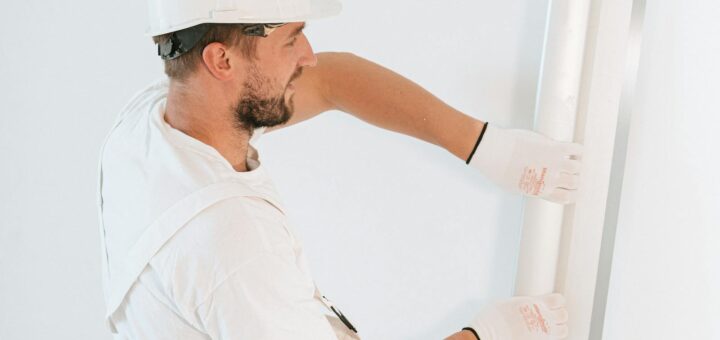 Professional construction worker installing drywall with gloves and helmet inside a building.